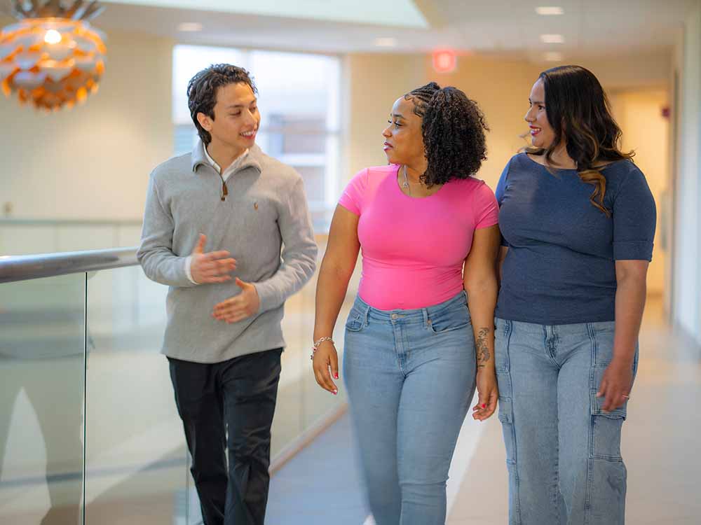 three students walking down hall together, chatting