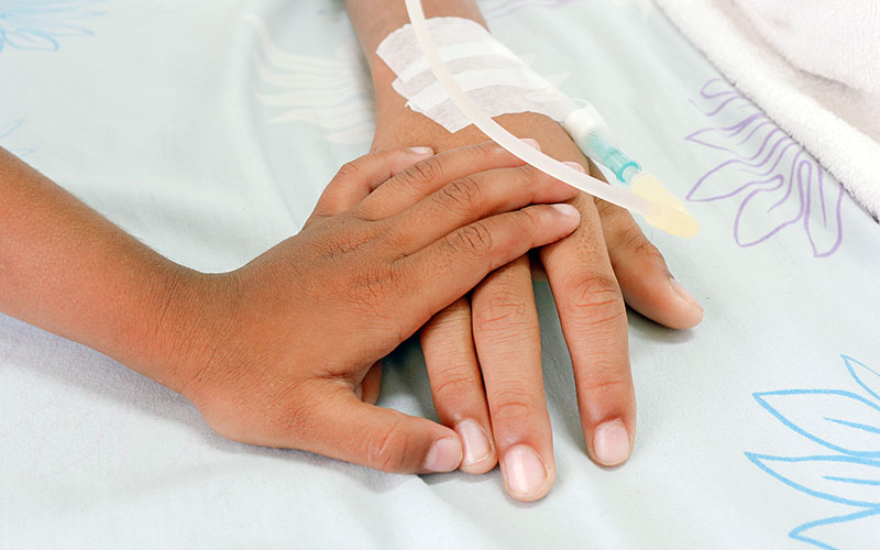 Child holding adult's hand in hospital bed